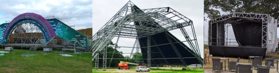 Outdoor festival stages under construction, featuring large metal frameworks and colorful designs, set on grassy fields with cloudy skies in the background