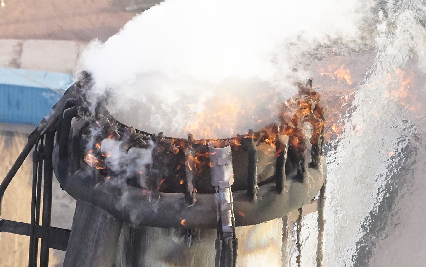 Industrial chimney with fire at the edge, emitting white smoke against a blurred background