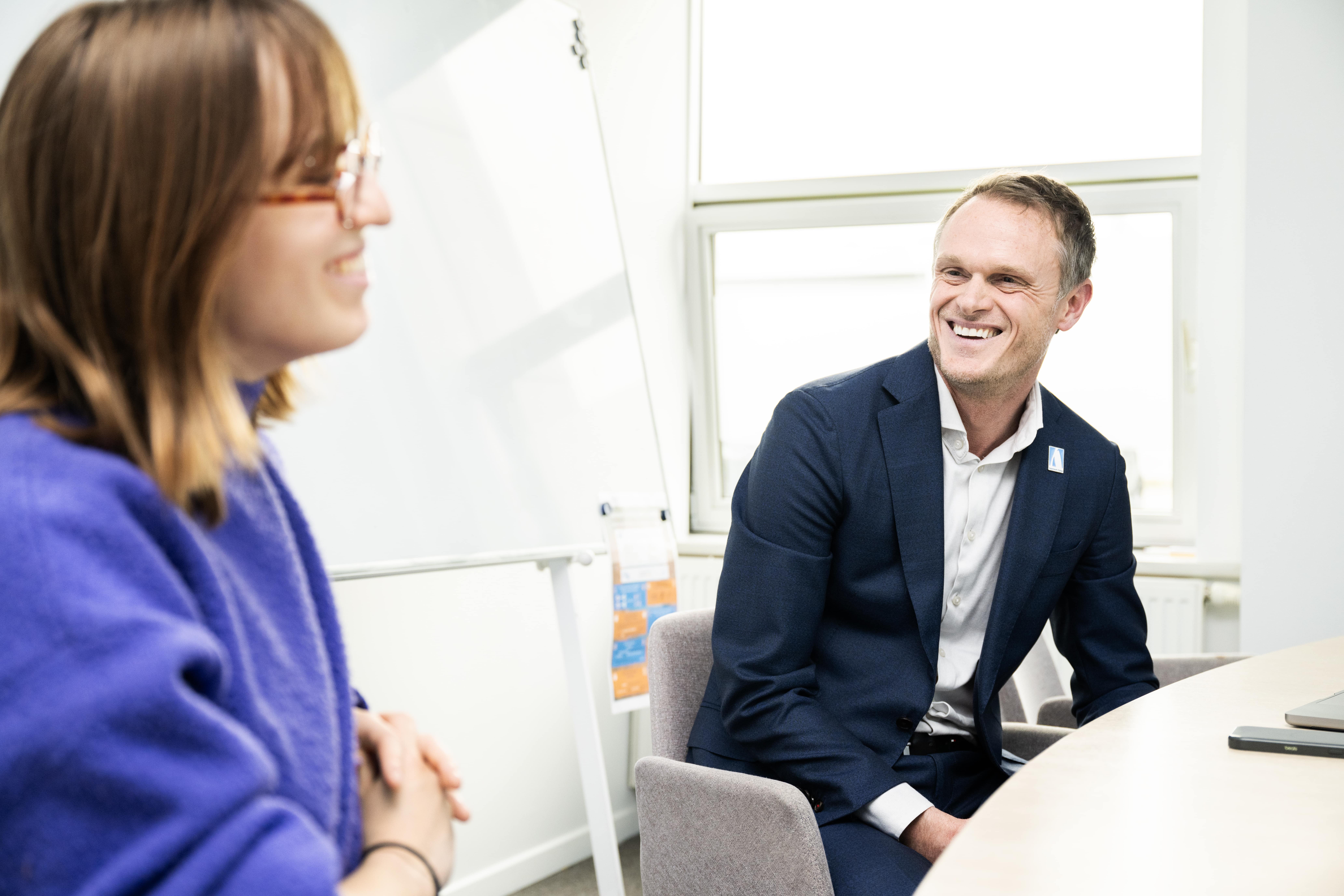 Man in a suit and woman in glasses having a friendly conversation in a bright office setting