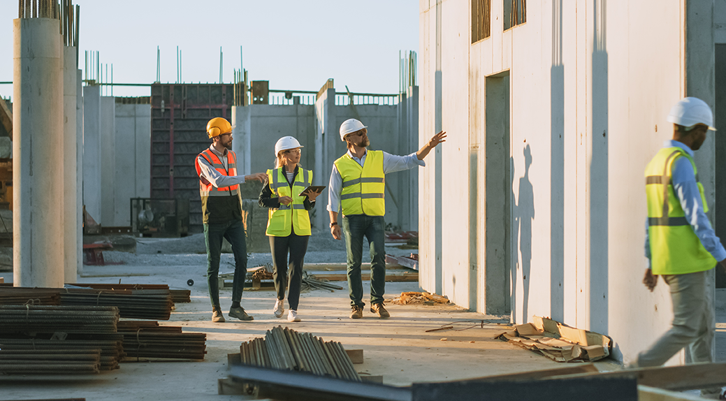 Construction site with three Kiwa inspectors wearing safety helmets and reflective vests inspecting concrete structures