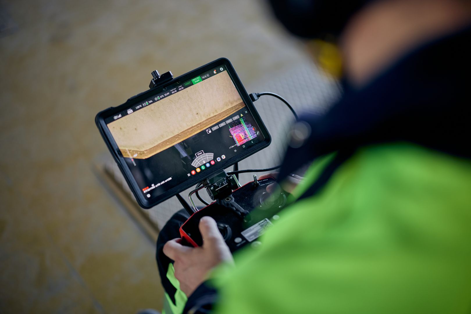 Kiwa auditor operating a drone with a handheld controller displaying live video feed on a screen, wearing a high-visibility jacket, focusing on inspecting a building interior