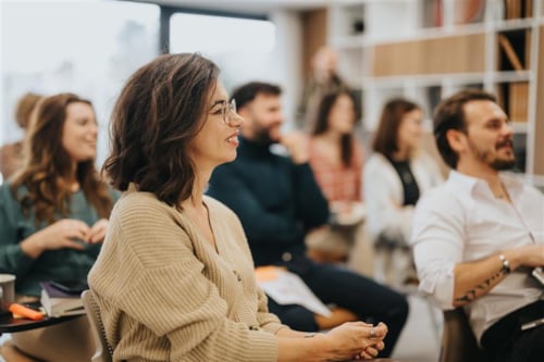A diverse group of adults attentively listening during a seminar or workshop, seated in a modern classroom setting