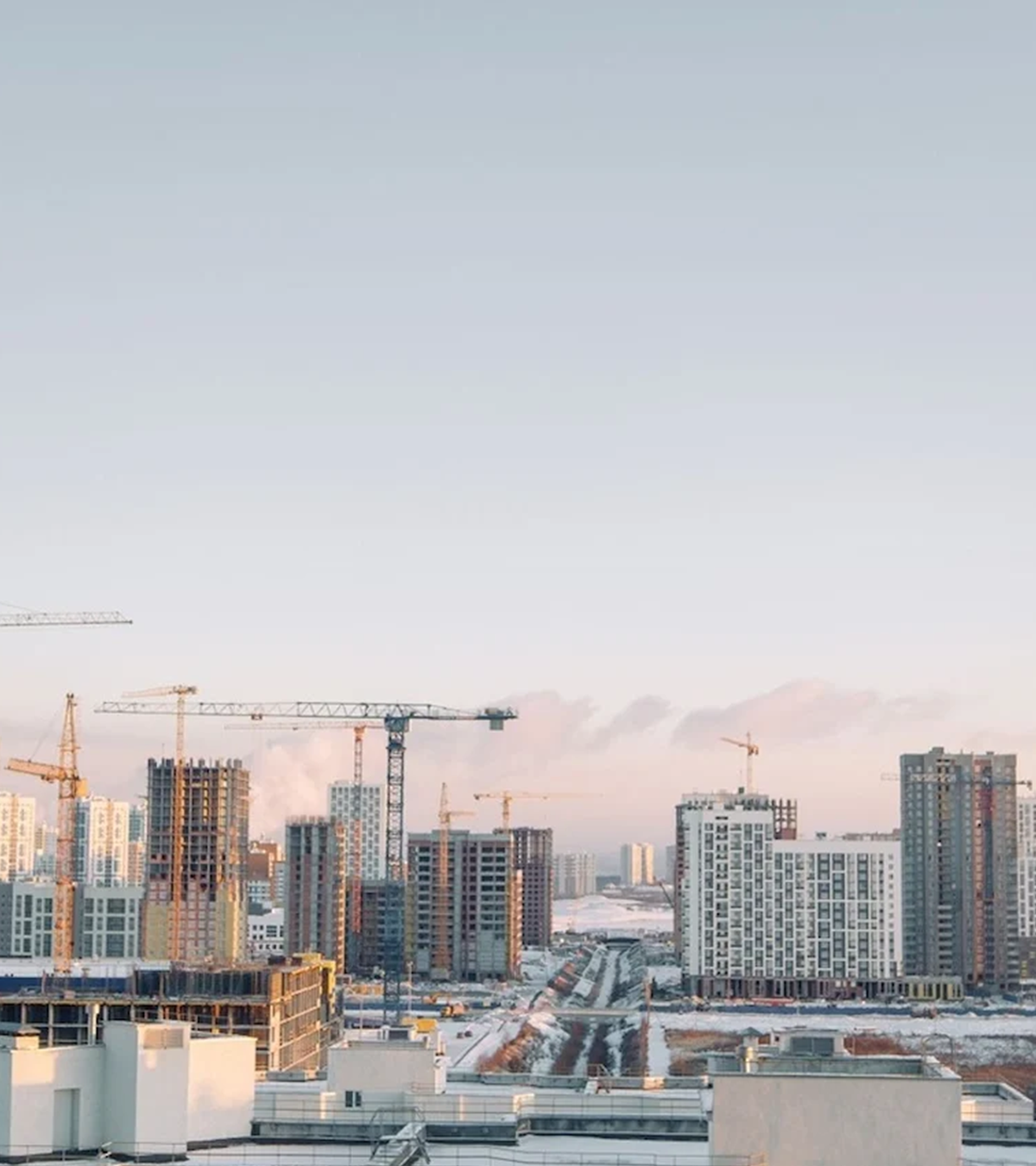 Urban skyline with high-rise buildings under construction and multiple cranes, set against a clear sky