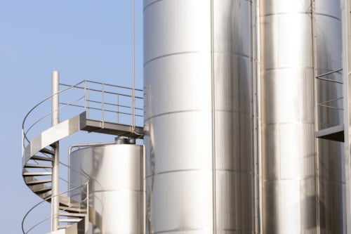 Kiwa inspected stainless steel industrial silos with a spiral staircase, against a clear blue sky, showcasing modern architectural design in industrial storage