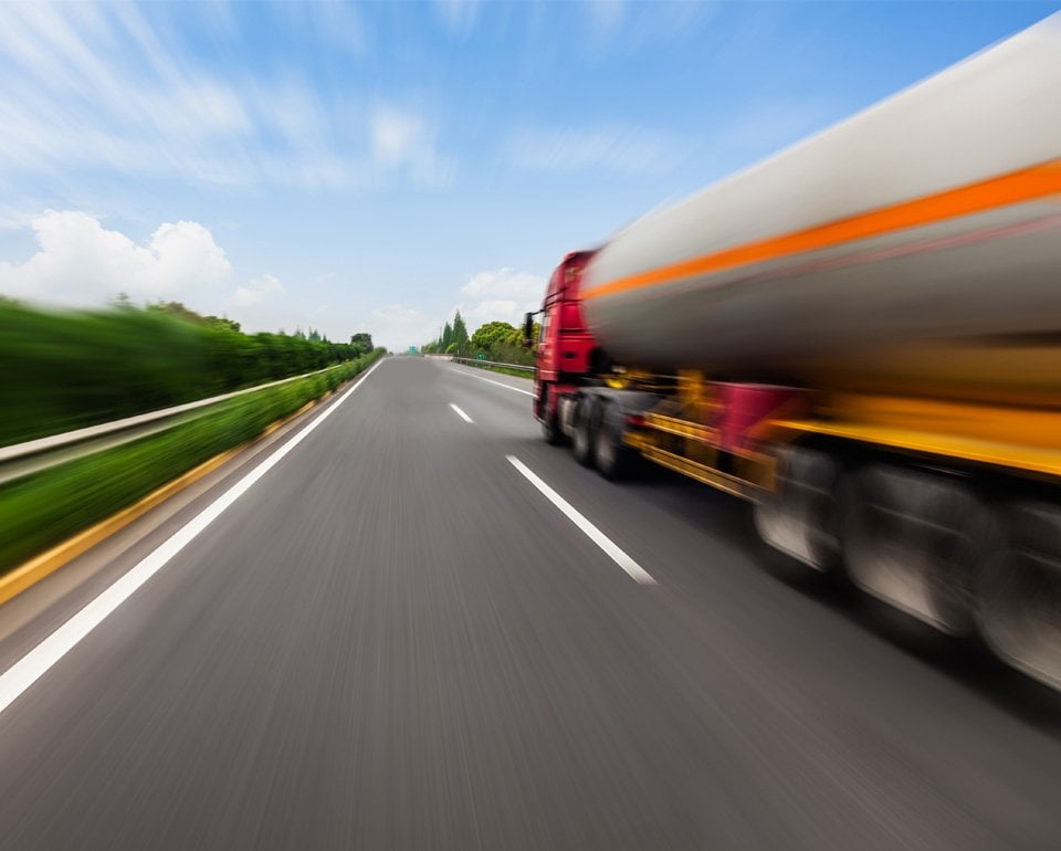 En tankbil susar fram på en rak landsväg, som sträcker sig långt fram mot horisonten. 