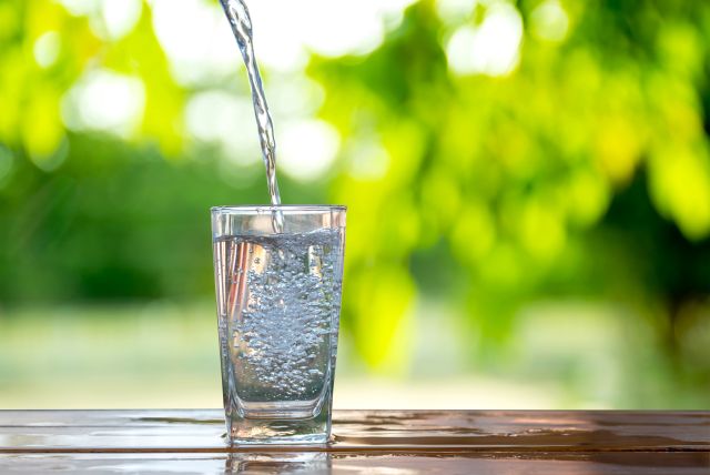 Glass of water being poured on a wooden table outdoors, with a green nature background