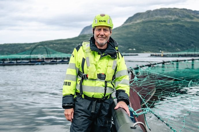 Kiwa auditor Freddy in high-visibility gear standing by aquaculture netting with mountainous backdrop