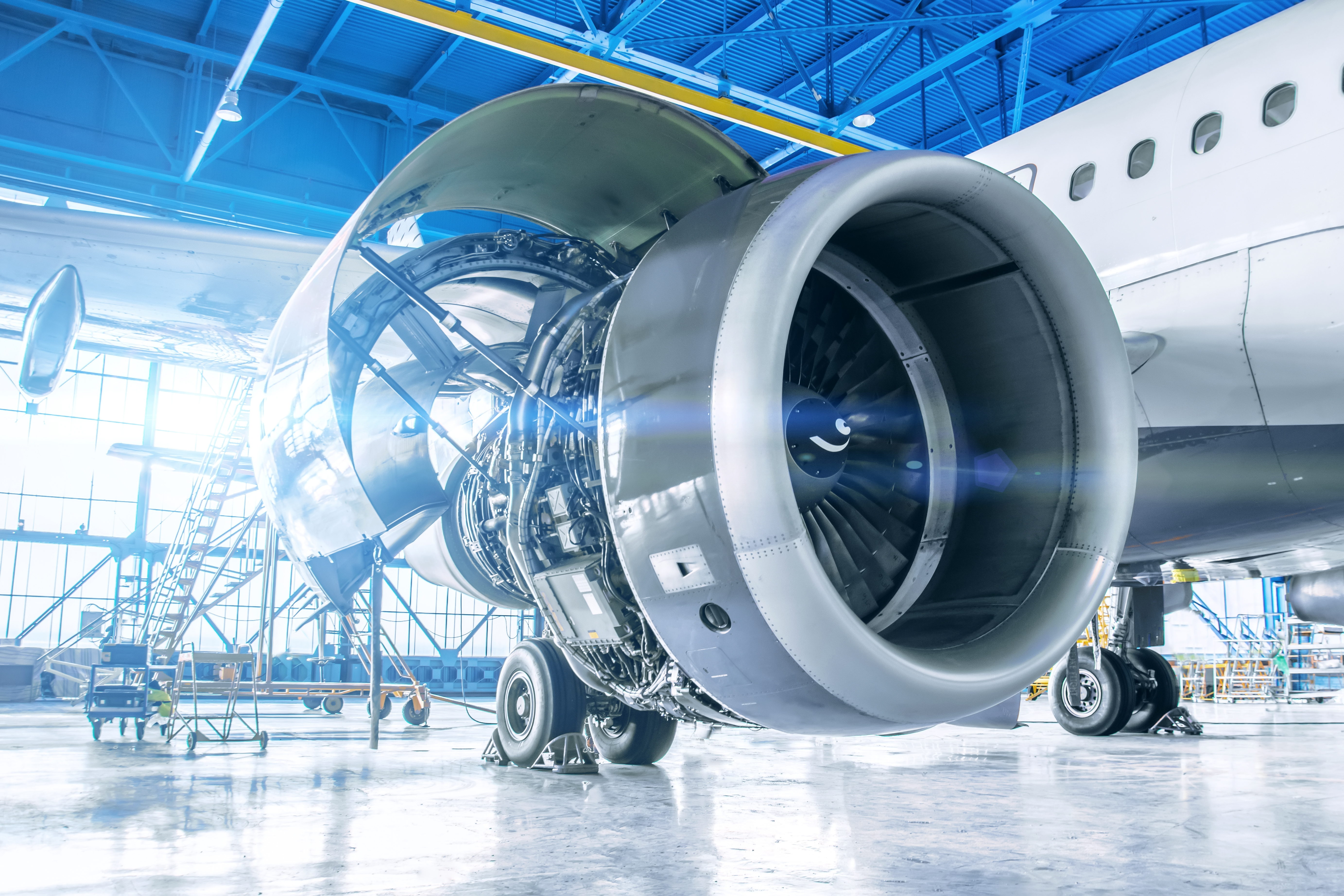 Commercial airplane jet engine undergoing maintenance in a hangar, showcasing detailed turbine and machinery components under natural light