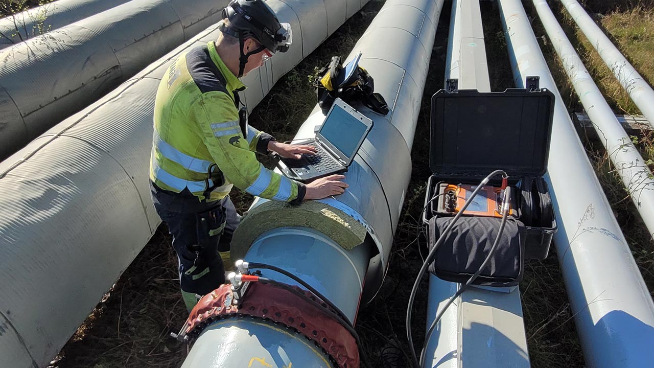 Kiwa technician in safety gear inspecting pipeline with laptop and equipment in an outdoor industrial setting