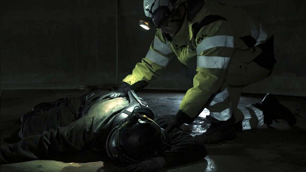 En medvetslös person ligger i mörket på marken , en kollega böjer sig över personen.