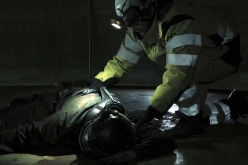 En medvetslös person ligger i mörket på marken , en kollega böjer sig över personen.