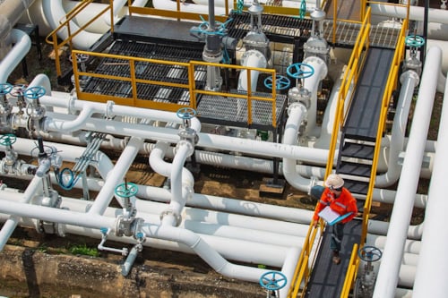 Tekniker inspekterar utomhus ventiler och rörledningar i en industri.