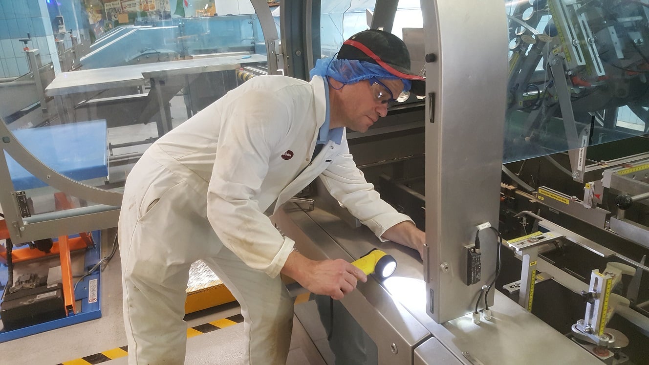Kiwa auditor in protective gear inspecting machinery in a factory setting with a flashlight