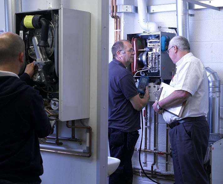 Kiwa trainer and student servicing and inspecting industrial boilers in a mechanical room during a class room course.