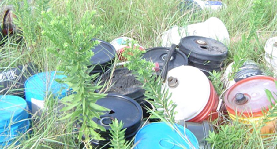Plastic containers and canisters discarded in a grassy field, highlighting environmental waste and pollution